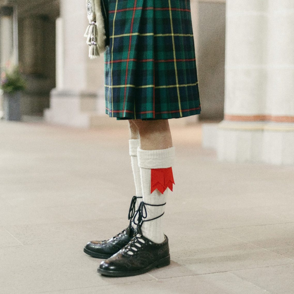 Beine eines Menschen in einem Kilt, traditionelle weiße Kniestrümpfe und schwarze Schuhe.